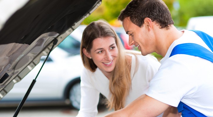 Woman talking to a car mechanic in a parking area, both are stan