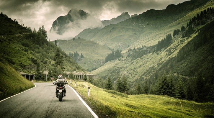 Motorcyclist on mountainous highway, cold overcast weather, Euro